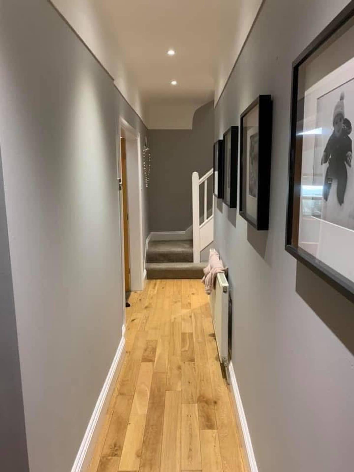 Hallway in warm grey with an oak floor and a run of framed photographs